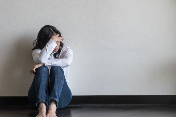 A young woman sitting on the floor against a wall, head in her hands