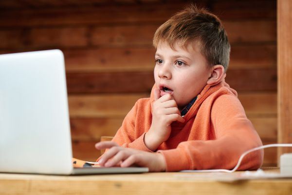 A young boy looking thoughtfully at a laptop